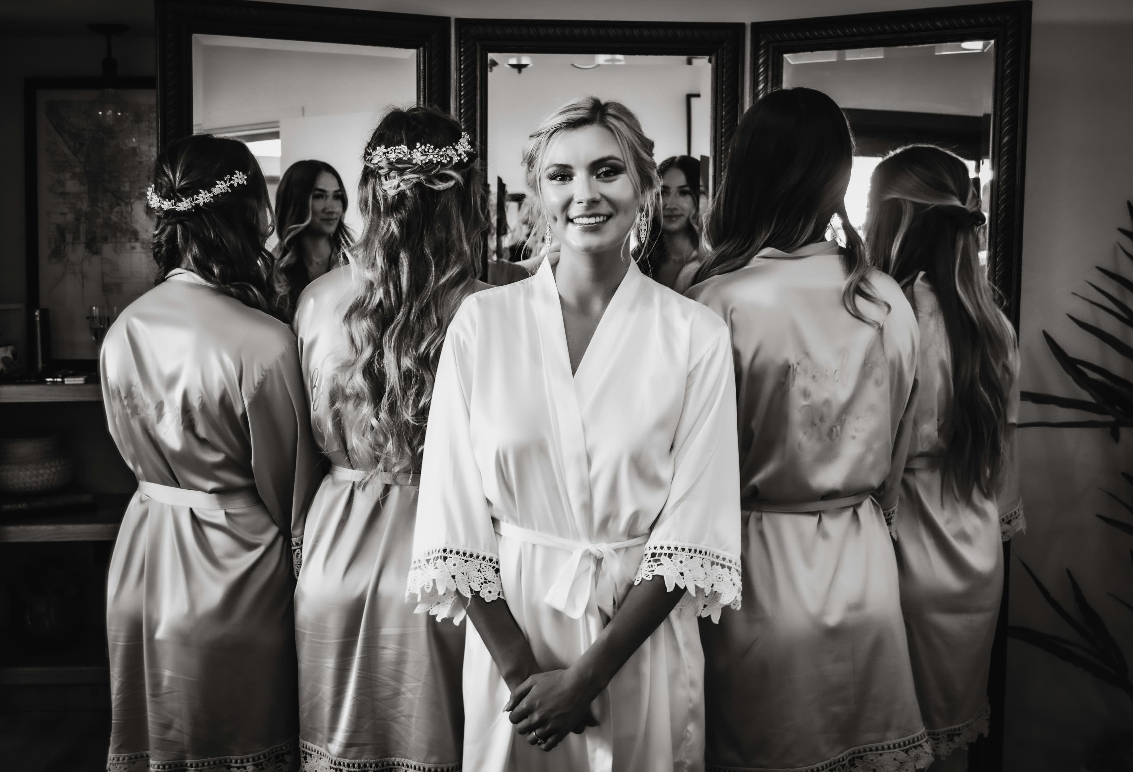 Bride in white lace robe with bridesmaids getting ready